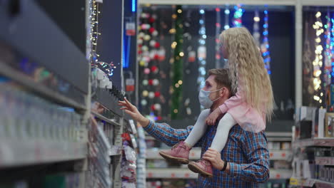 Father-and-daughter-on-shoulders-choose-Christmas-garlands-for-Christmas-in-the-supermarket